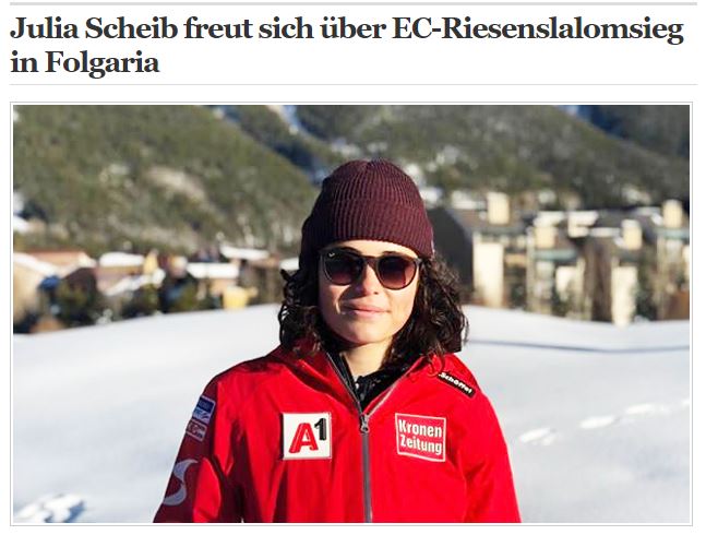 Das Bild zeigt ein Portrait von Julia Scheib in roter Jacke vor einer Stadt stehend.